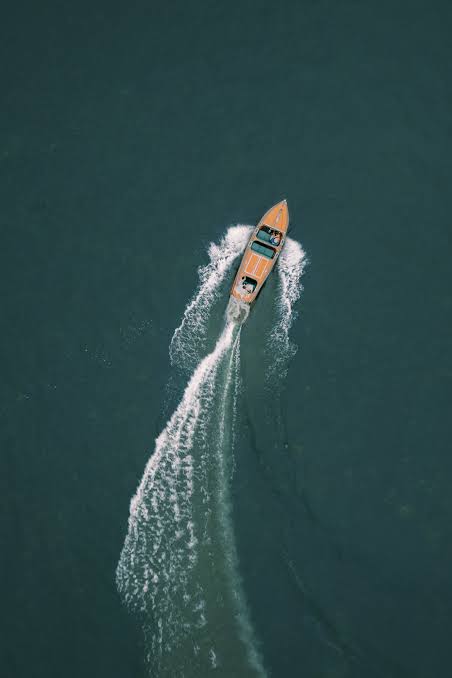 Aerial drone photo of a wooden runabout cutting a white wake across dark green water
